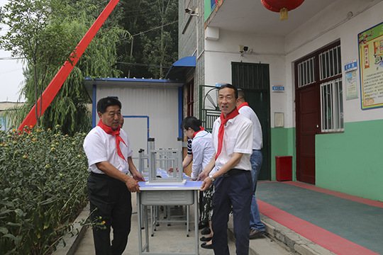 集團公司領(lǐng)導與學(xué)生一起將桌椅搬進(jìn)教室
